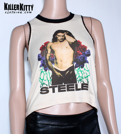 Women's Peter Steele relaxed fit, slouchy tank top. Type O Negative Top is tan/beige color, Asymmetrical hem, black lace-edged arms and black crew neck with an image of Peter Steele's Playgirl Cover. Band shirt.  Killer Kitty Clothing Alternative Brand. Mannequin wearing a sleeveless top with a graphic design and 'STEELE' text on a tan background