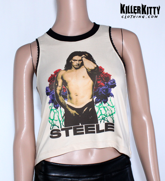 Women's Peter Steele relaxed fit, slouchy tank top. Type O Negative Top is tan/beige color, Asymmetrical hem, black lace-edged arms and black crew neck with an image of Peter Steele's Playgirl Cover. Band shirt.  Killer Kitty Clothing Alternative Brand. Mannequin wearing a sleeveless top with a graphic design and 'STEELE' text on a tan background