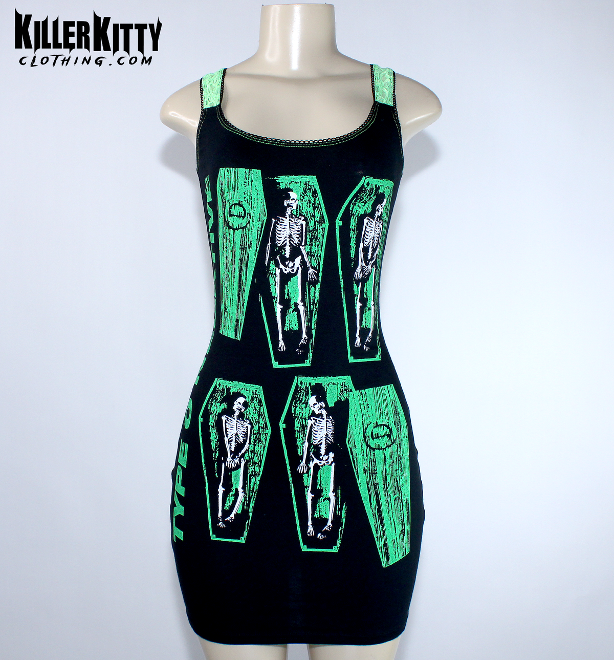 A sleeveless black mini dress with bright green trim and a graphic print of skeleton figures inside coffin shapes, displayed on a  mannequin. Type O negative dress for women. goth metal bodycon dress. peter steele goth metal dress. women's type o negative shirt. upcycled type o negative dress. heavy metal type o negative bodycon dress. diy alternative type o negative dress. killer kitty clothing upcycled band dresses. goth horror skeleton dress for women. alt fashion brand killer kitty. band dress for women