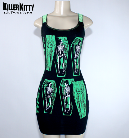 A sleeveless black mini dress with bright green trim and a graphic print of skeleton figures inside coffin shapes, displayed on a  mannequin. Type O negative dress for women. goth metal bodycon dress. peter steele goth metal dress. women's type o negative shirt. upcycled type o negative dress. heavy metal type o negative bodycon dress. diy alternative type o negative dress. killer kitty clothing upcycled band dresses. goth horror skeleton dress for women. alt fashion brand killer kitty. band dress for women